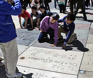 Tourists compare hand prints with a celebrity in the courtyard of the Chinese Theatre Courtyard on Hollywood Boulevard. [Photo Credit: LAtourist.com]